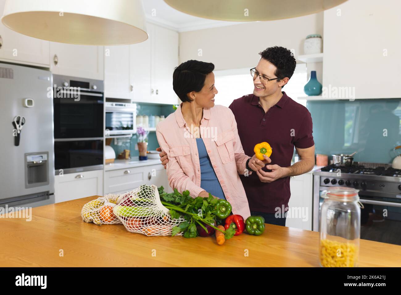 Happy diverse couple cooking dinner together, smiling and embracing in kitchen Stock Photo
