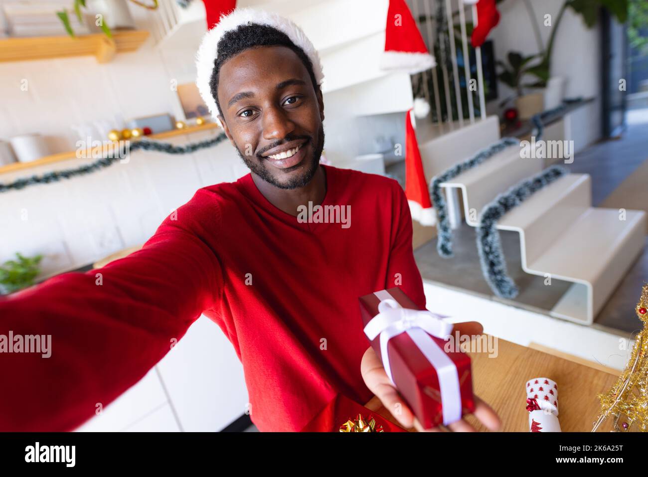 Happy african american man wearing santa claus hat, holding present and ...