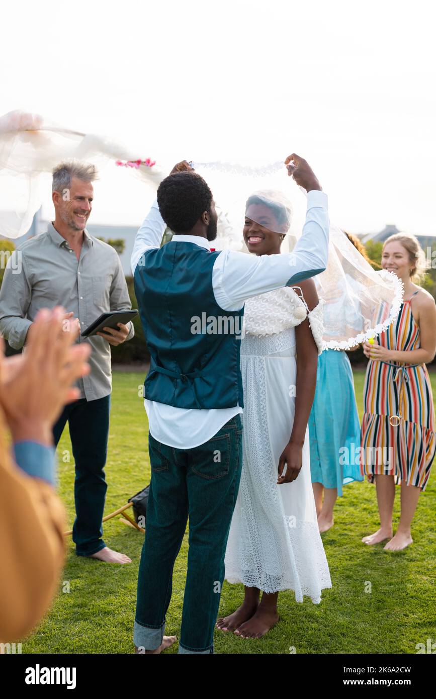 Happy african american couple holding veil and smiling during wedding ...