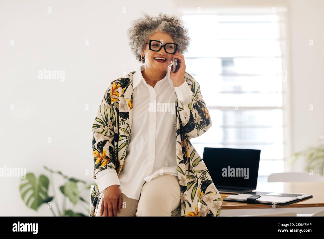 Cheerful businesswoman smiling happily while speaking with her business partners on a phone call. Mature businesswoman making business plans while sit Stock Photo