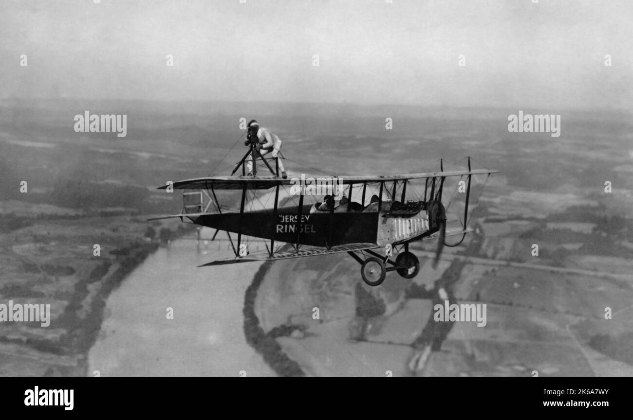 Aerial barnstormer standing with his camera on top of the wing of a biplane in flight, 1921. Stock Photo