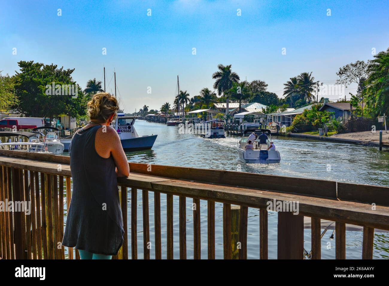 Woman watches from pier of crowded canal with partying boaters near Phuzzy's Boat Shack restaurant & bar in St. James City, Pine Island, FL Stock Photo
