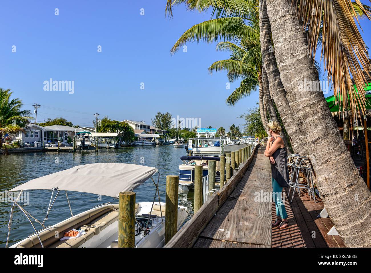 Woman viewing canal boat traffic and boats docked alongside Phuzzys Boat Shack restaurant & bar in St. James City, Pine Island, FL Stock Photo