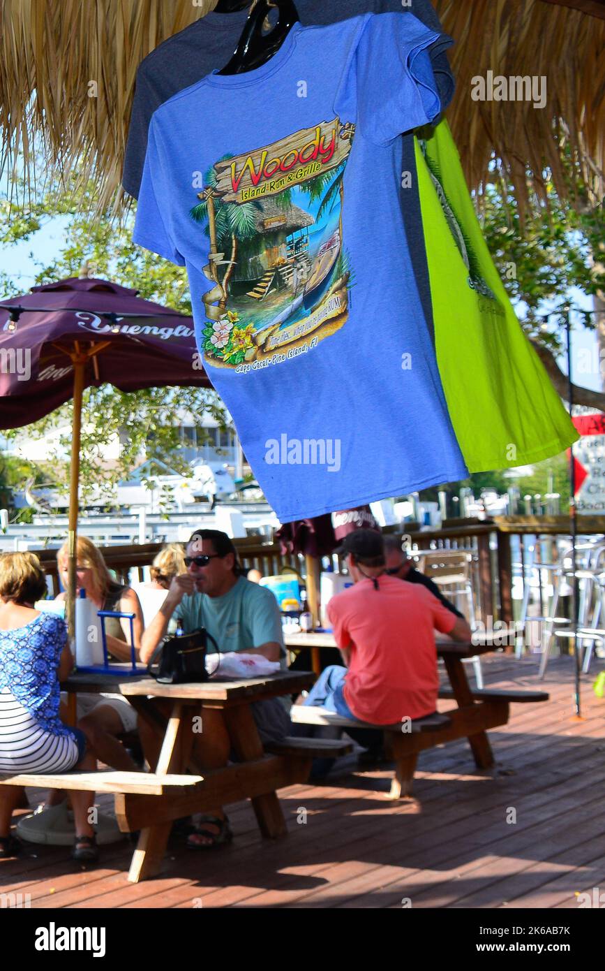 Tee-shirts for sell under a thatched roof for People enjoying outdoor dining at Phuzzy's Boat Shack Restaurant on the canal in Saint James City, FL on Stock Photo