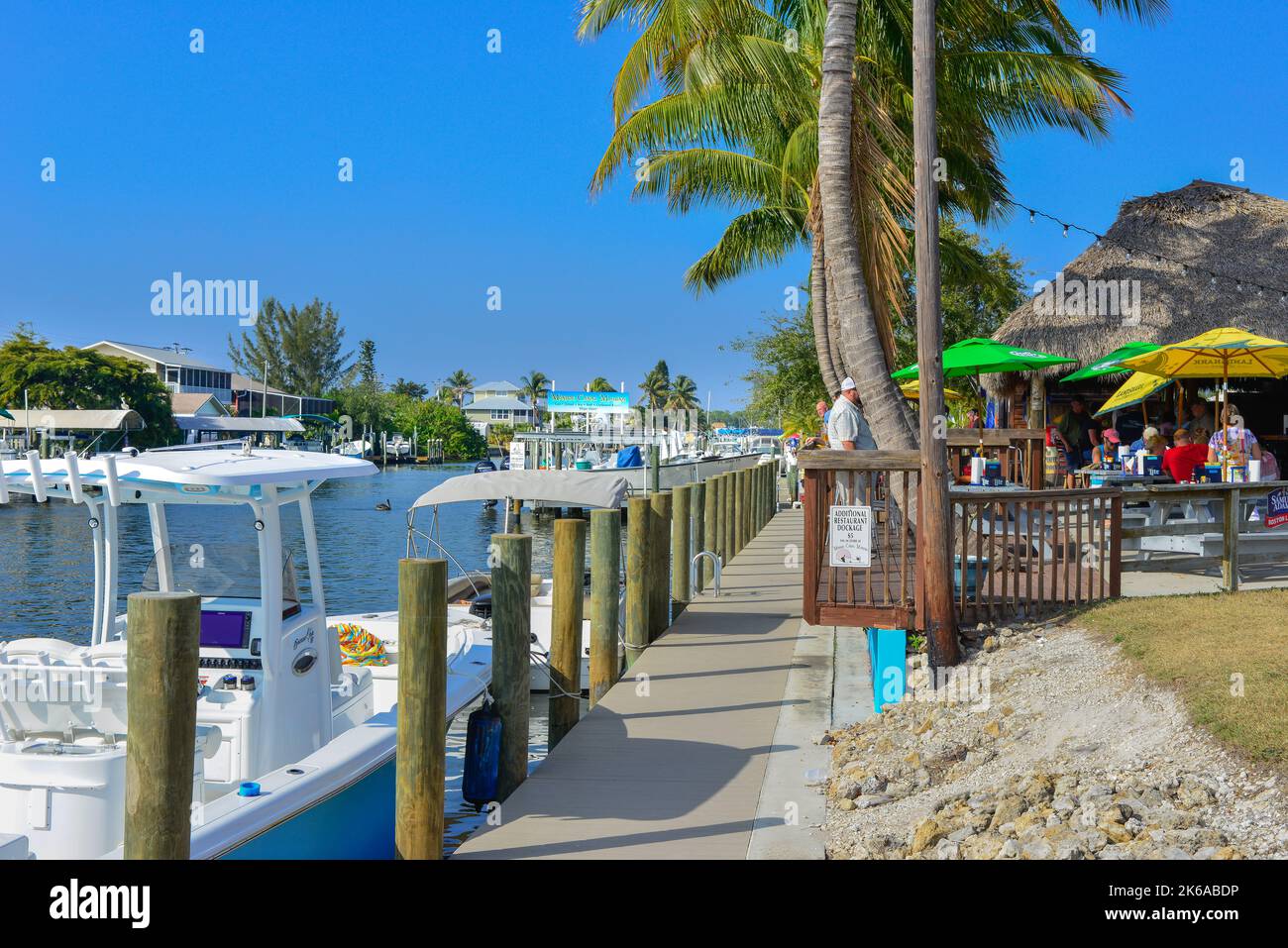 A view of the canals with docked boats, alongside Phuzzy's Boat Shack restaurant and bar with thatched roofs and outdoor dining in St. James City, FL, Stock Photo