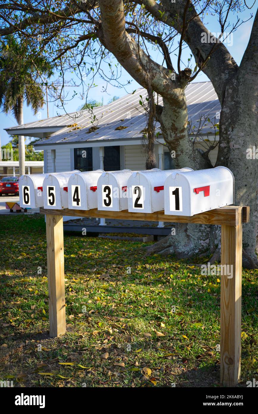 A simplistic yet graphic presentation of six identical mailboxes in a row with homemade wooden stand, and large stick-on numbers, one through six in B Stock Photo