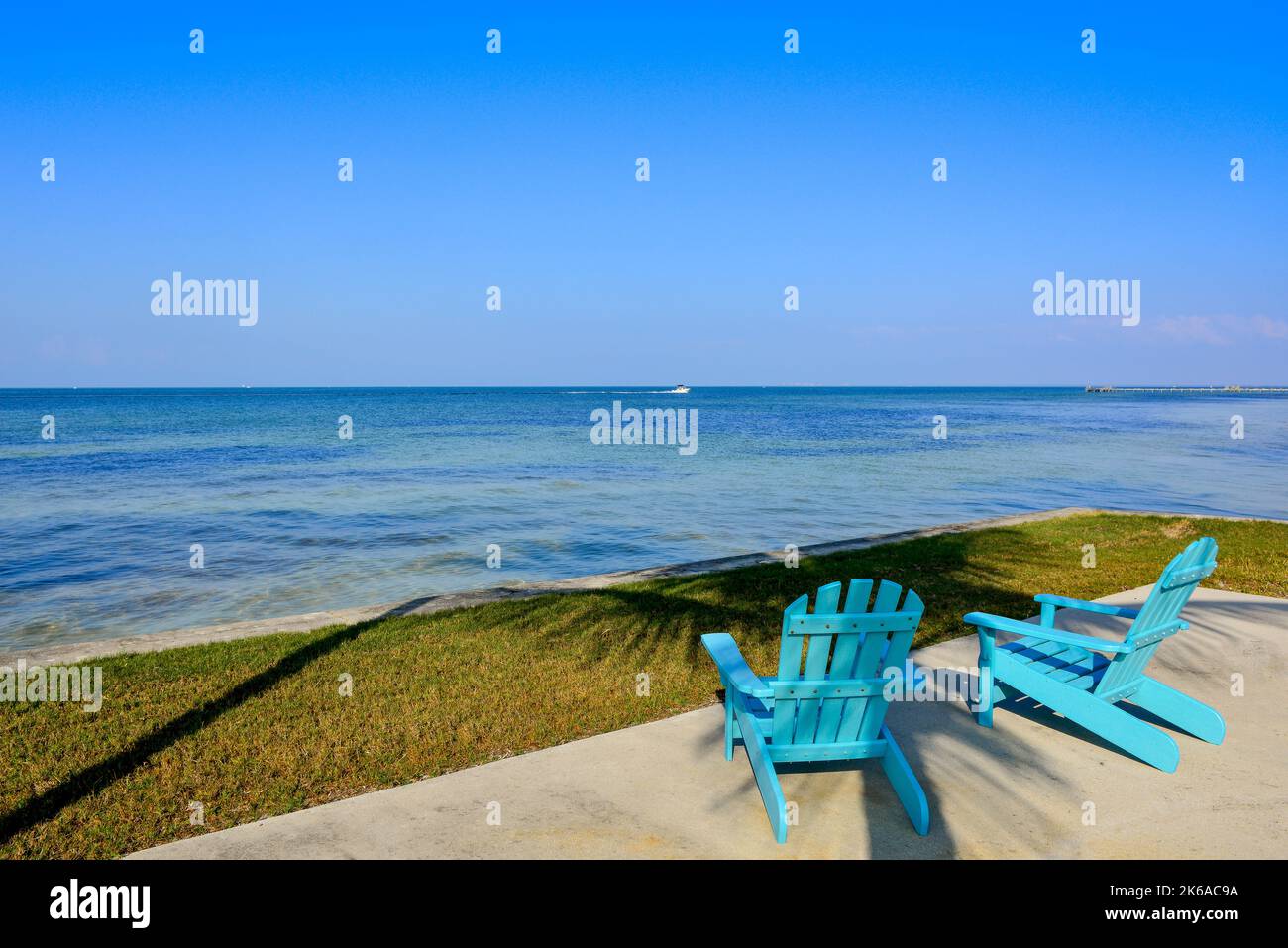 Rear view of turquoise blue Adirondack style chairs outside at waterfront  on Charlotte Harbor with wide view of blue sky & water, Bokeelia, FL Stock Photo