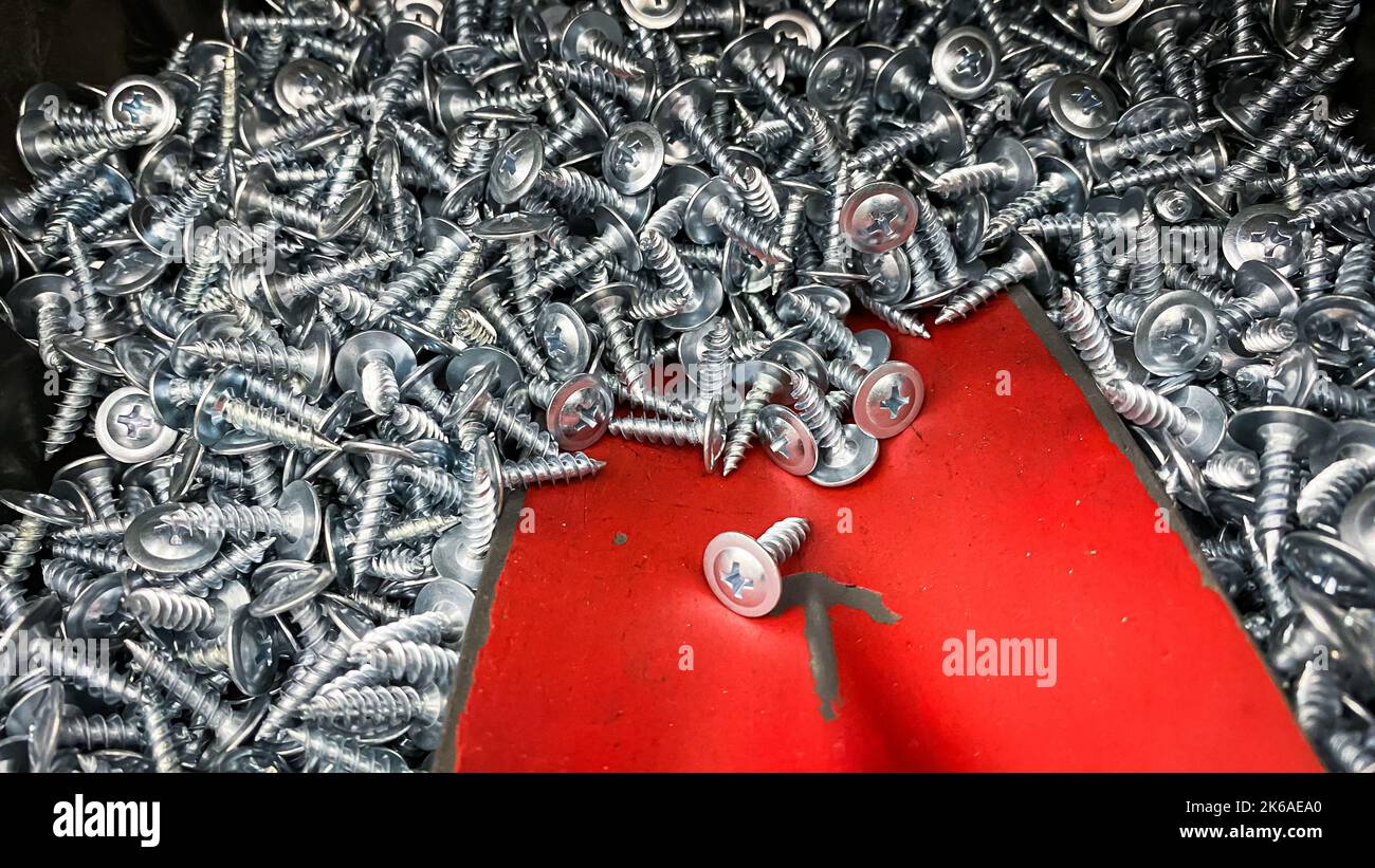 Red spatula picking up metal stainless steel screws.Shiny short self