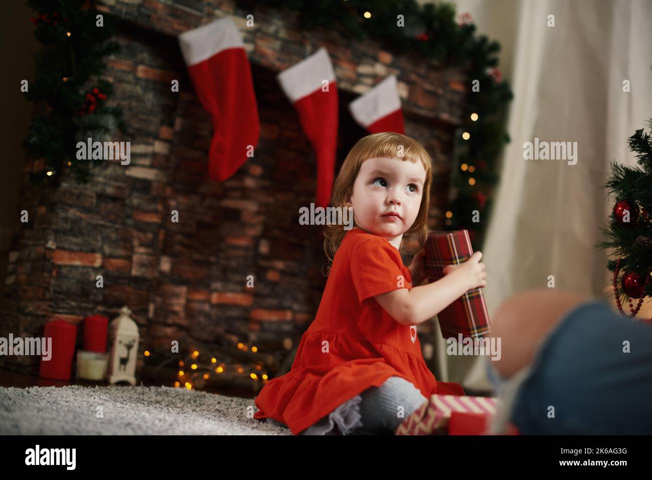 Giving gifts. Little girl with Christmas gifts by the fireplace Stock Photo
