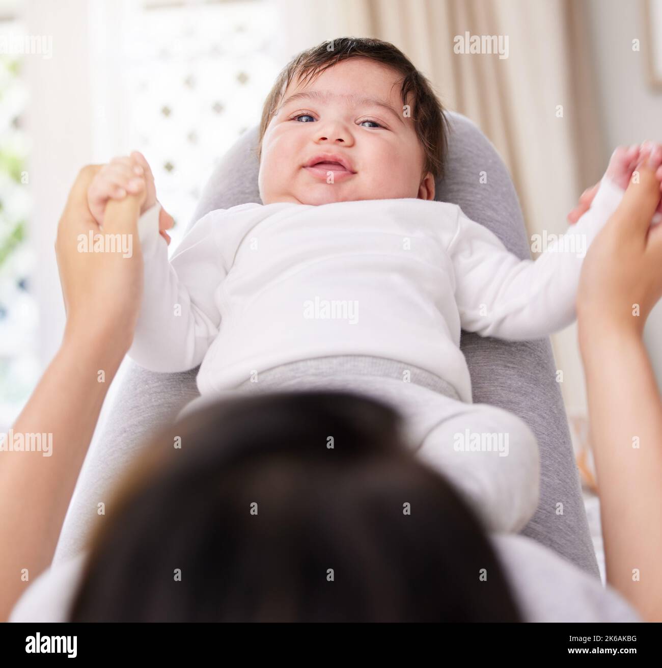 Mother playing with her newborn baby girl at home. Little baby lying on her mothers legs. Woman holding her small childs arms open, playing with her Stock Photo