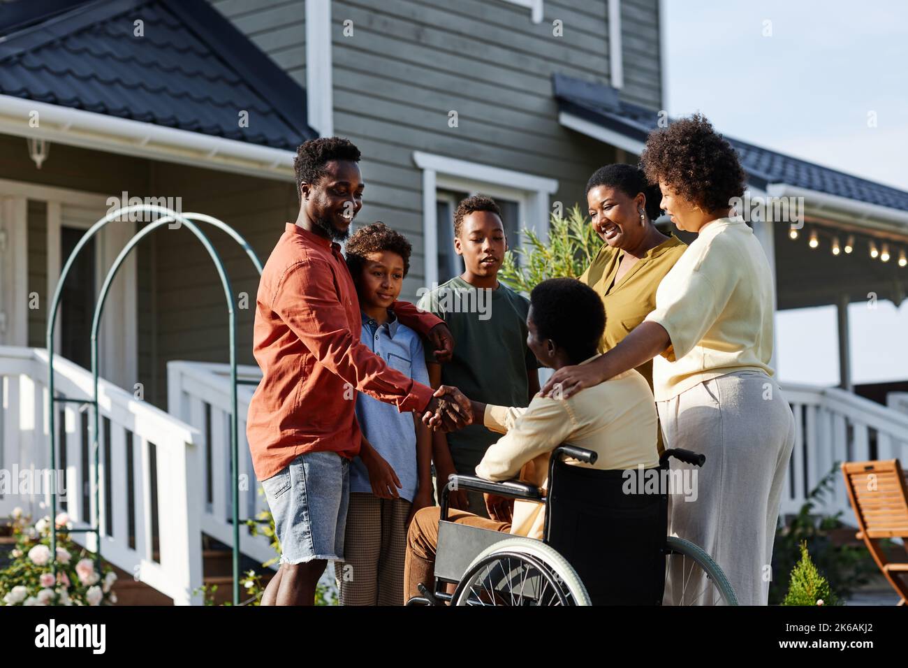 Portrait of big African American family with person in wheelchair standing outdoors by house