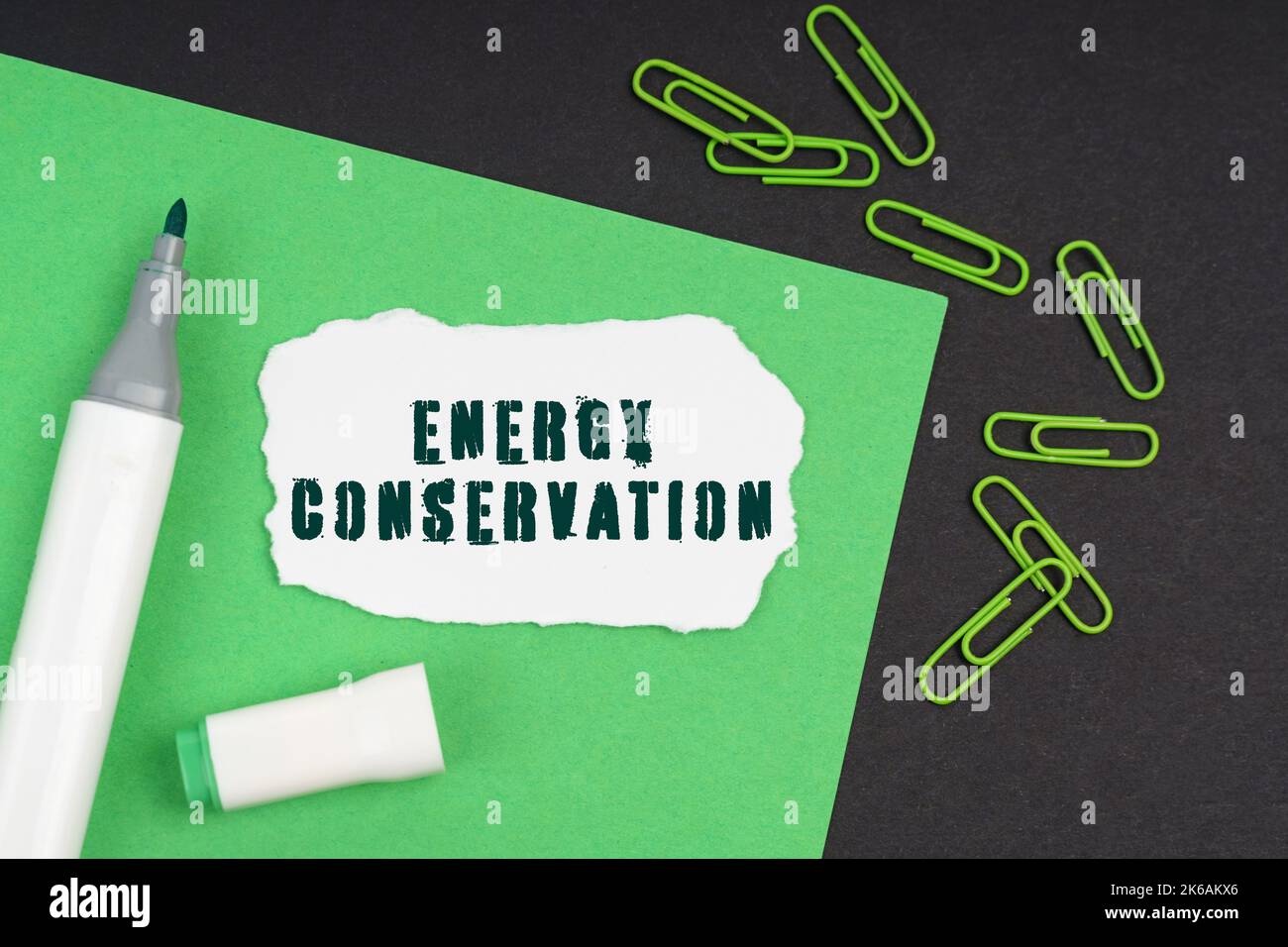 Ecology concept. On a black background, a marker, paper clips, a sheet and torn paper with the inscription - Energy Conservation Stock Photo