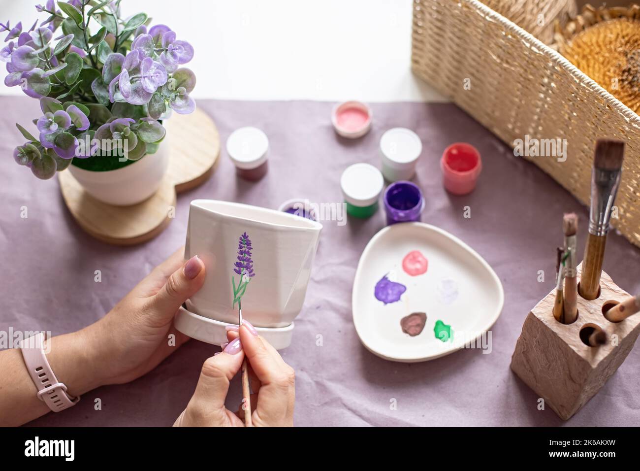 Womens hands paint a white flower ceramic pot on the table. Top view Stock Photo