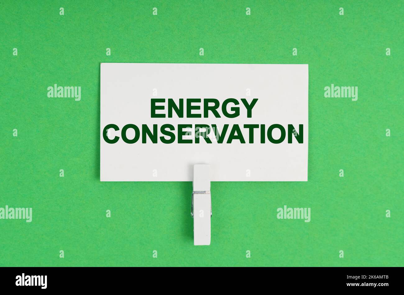 Ecology concept. On a green background, a business card on a clothespin. The business card says - Energy Conservation Stock Photo