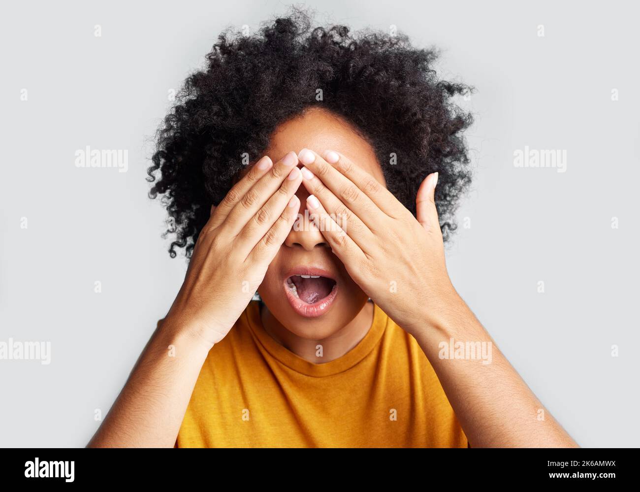 I want to peek so badly. a young woman covering her eyes while posing against a grey background. Stock Photo