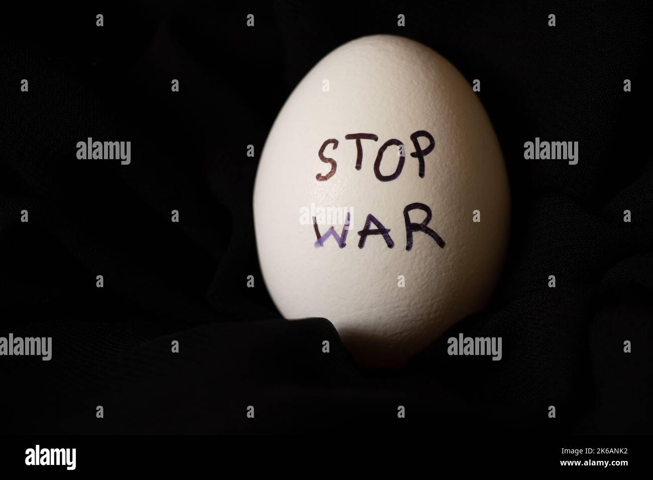 White chicken egg with the inscription stop the war , which lies on a black background, food and war in Ukraine 2022 Stock Photo