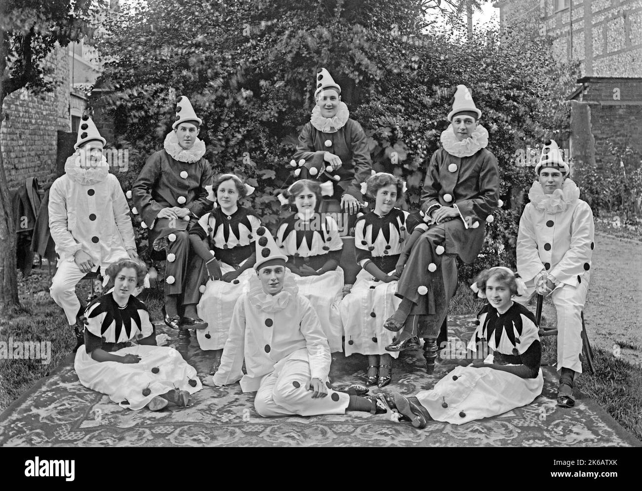 A group of men and women wearing Pierrot (clown) costumes, Norfolk, England, UK c. 1930. A Pierrot is a character of pantomime and commedia dell’arte, whose origins are in the late seventeenth-century Italian troupe of players performing in Paris and known as the Comédie-Italienne. This is taken from an old black and white negative – a vintage 1920s/30s photograph. Stock Photo
