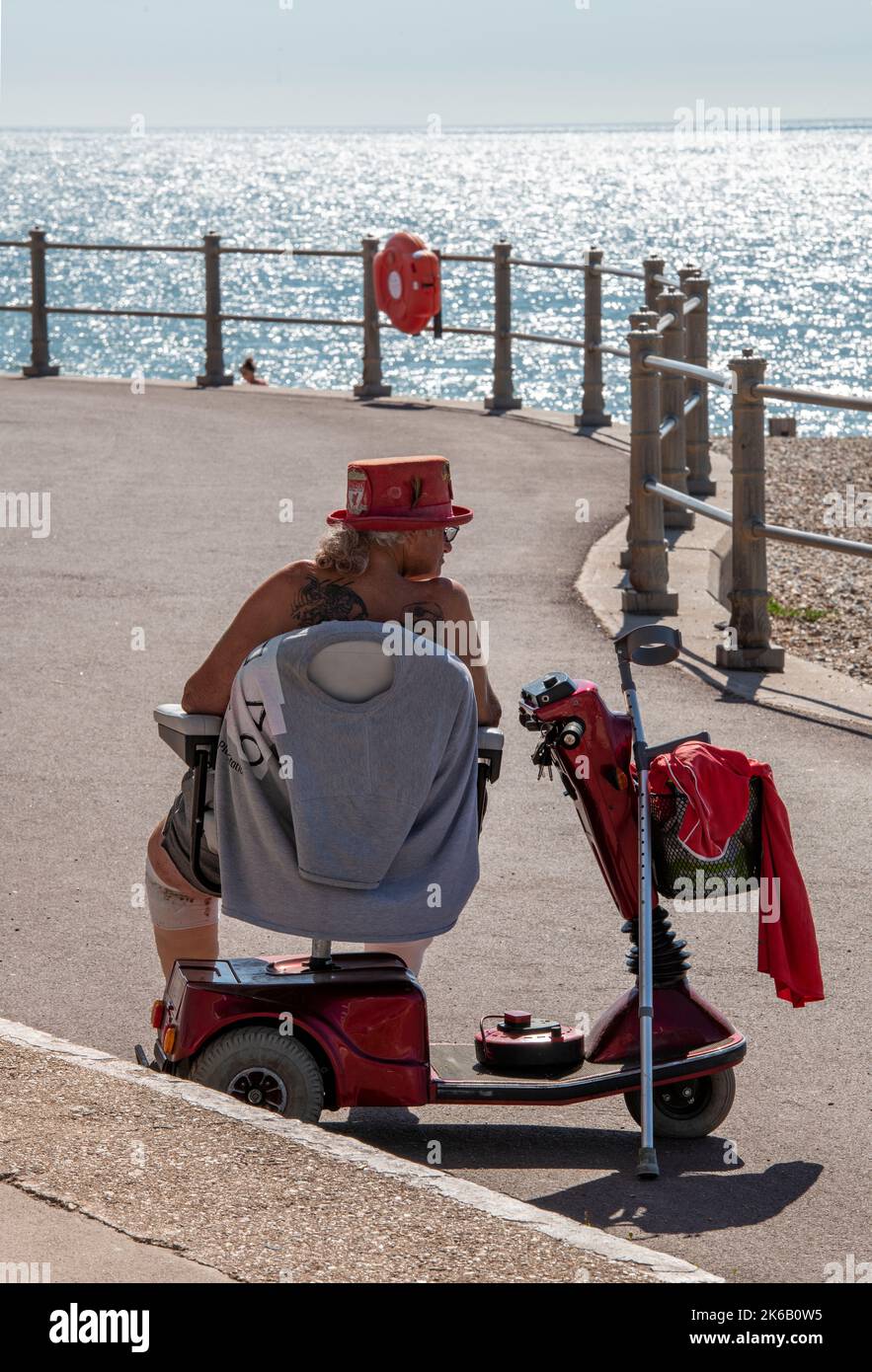 older lady in a wheelchair at the seaside on a mobility scooter enjoying the sunshine on a summers day at the coast. Stock Photo