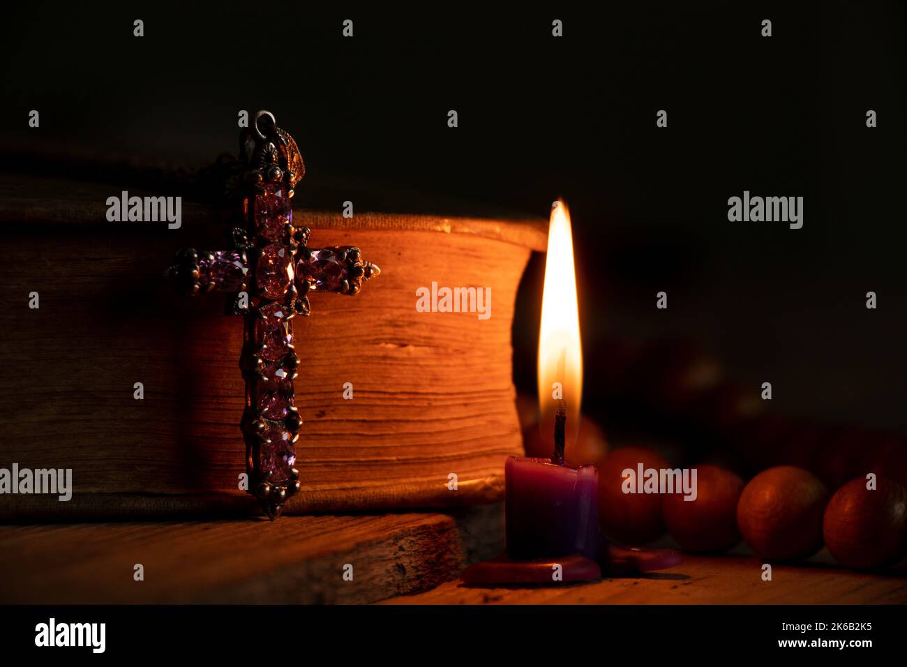 A bible cross and a wooden rosary lie on the table next to candles