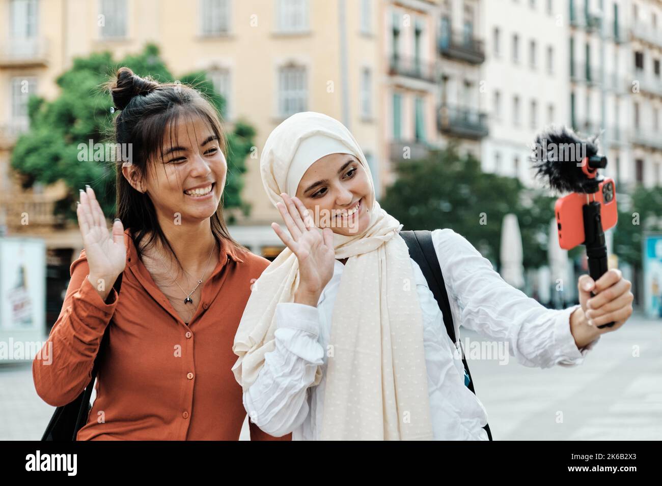 Multiethnic friends smiling and waving hand while streaming with a mobile phone outdoors on the