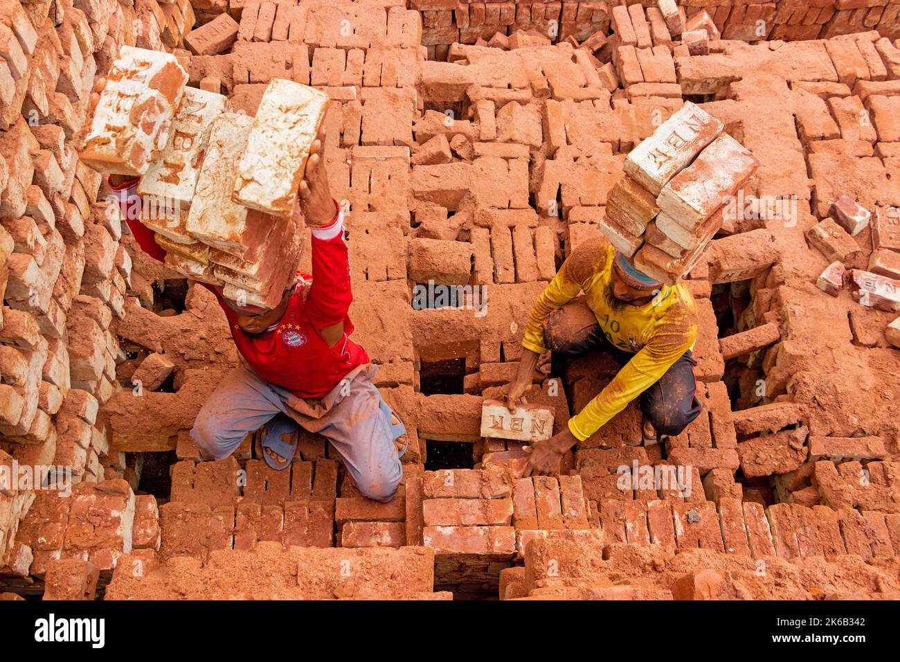 Dhaka, Dhaka, Bangladesh. 13th Oct, 2022. Workers in Dhaka, Bangladesh, carry piles of bricks weighing more than 15 kg on their heads as they are laid out ahead of being baked in a kiln. The labourers ""“ who are paid less than Â£1 a shift ""“ move up to 1,500 bricks a day in sweltering conditions. Around 4, 00,000 low-income migrants arrive in Dhaka from different parts of the country every year to work at brickfields. Long working hours under the scorching sun in the brick fields, massive accumulation of dust, the risk of falling from the trucks and piles of bricks, and carrying excessive l  Stock Photo