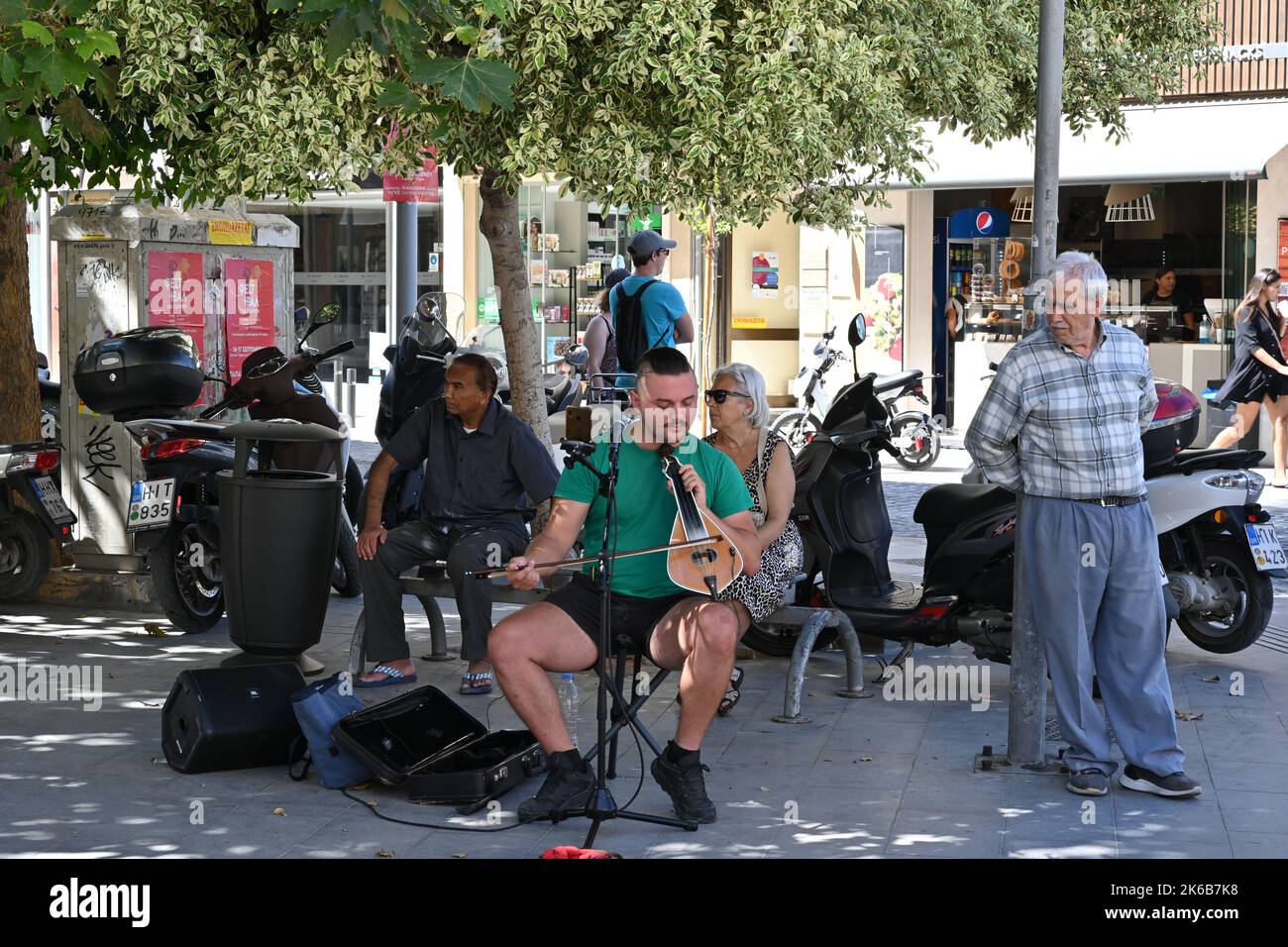 Street musician singing and playing Cretan lyra, traditional Greek music instrument in centrum of town surrounded by people. Stock Photo