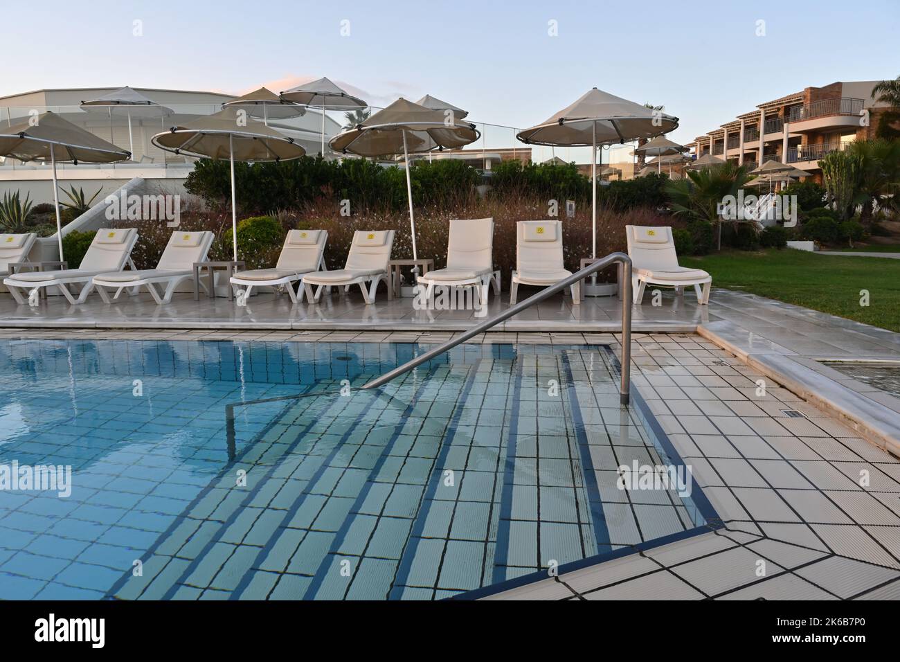 View from edge of the swimming pool on plastic deck chairs and straw beach umbrellas in Holiday resort TUI Magic Life Candia Maris. Stock Photo