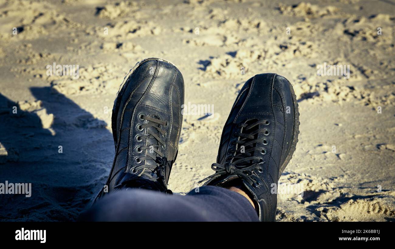 Black men's shoes laced up to the very top with sandy beaches in the background Stock Photo