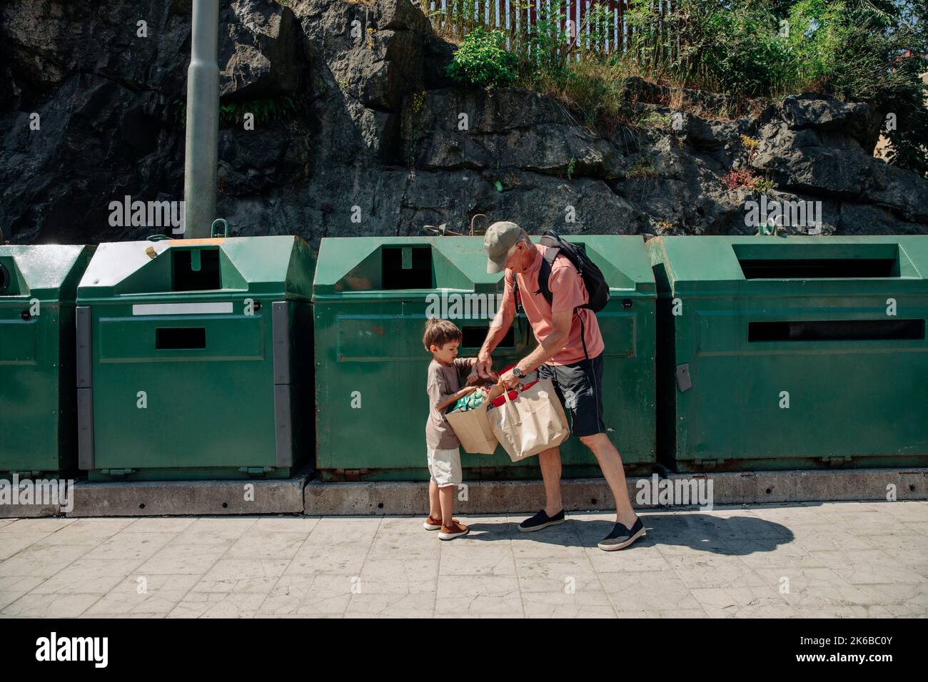 Grandfather and grandson holding garbage bags in front of bins Stock Photo