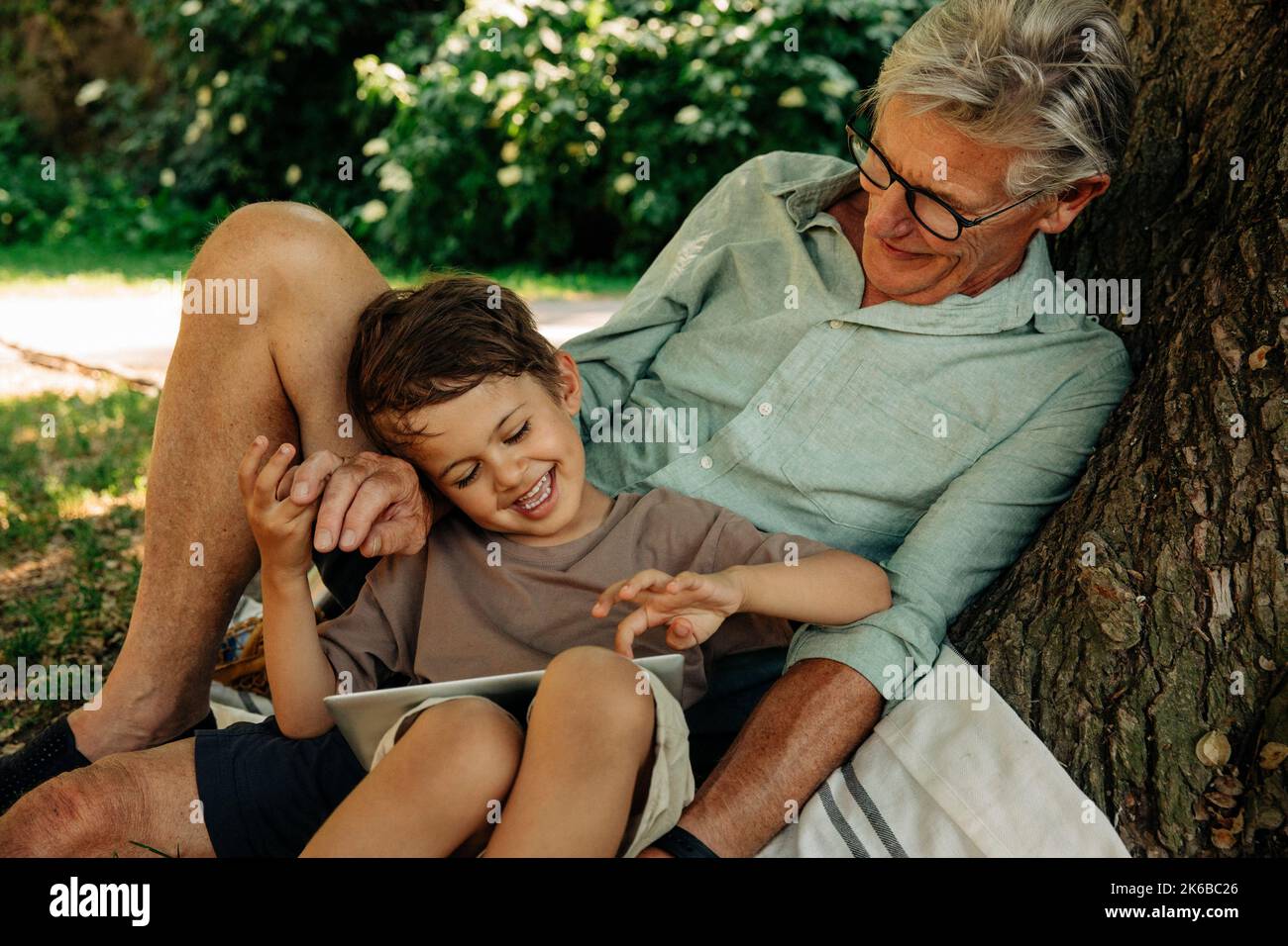 Boy using digital tablet while sitting with grandfather at park Stock Photo