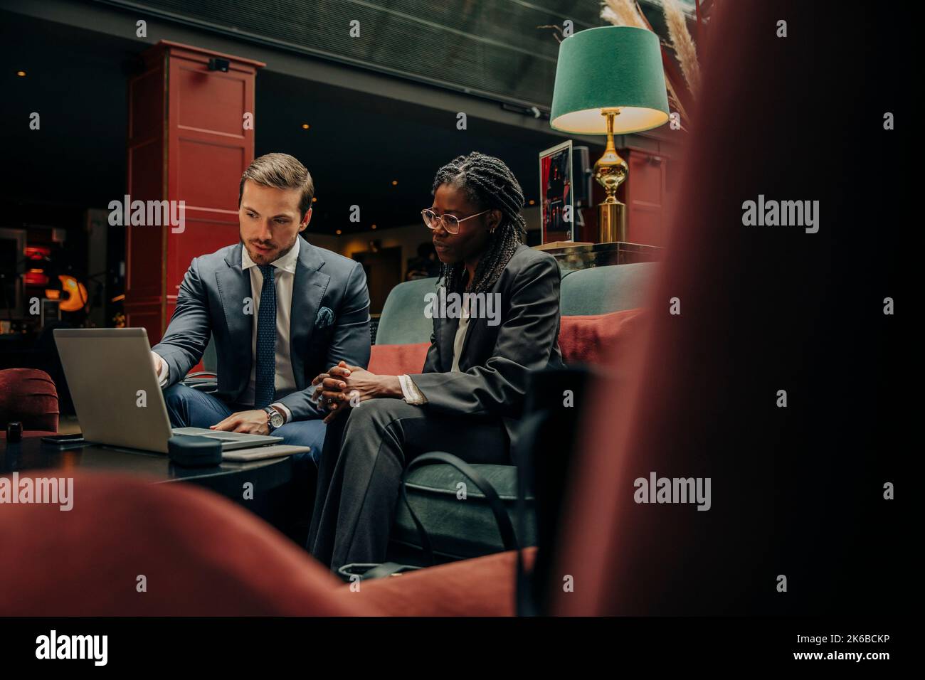 Young businessman discussing over laptop with female colleague sitting in hotel lounge Stock Photo