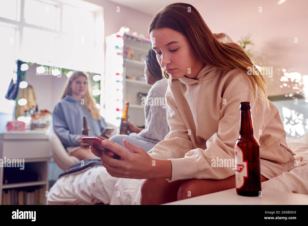 Group Of Teenage Girls In Bedroom Drinking Bottles Of Beer And Looking At Mobile Phones Stock Photo