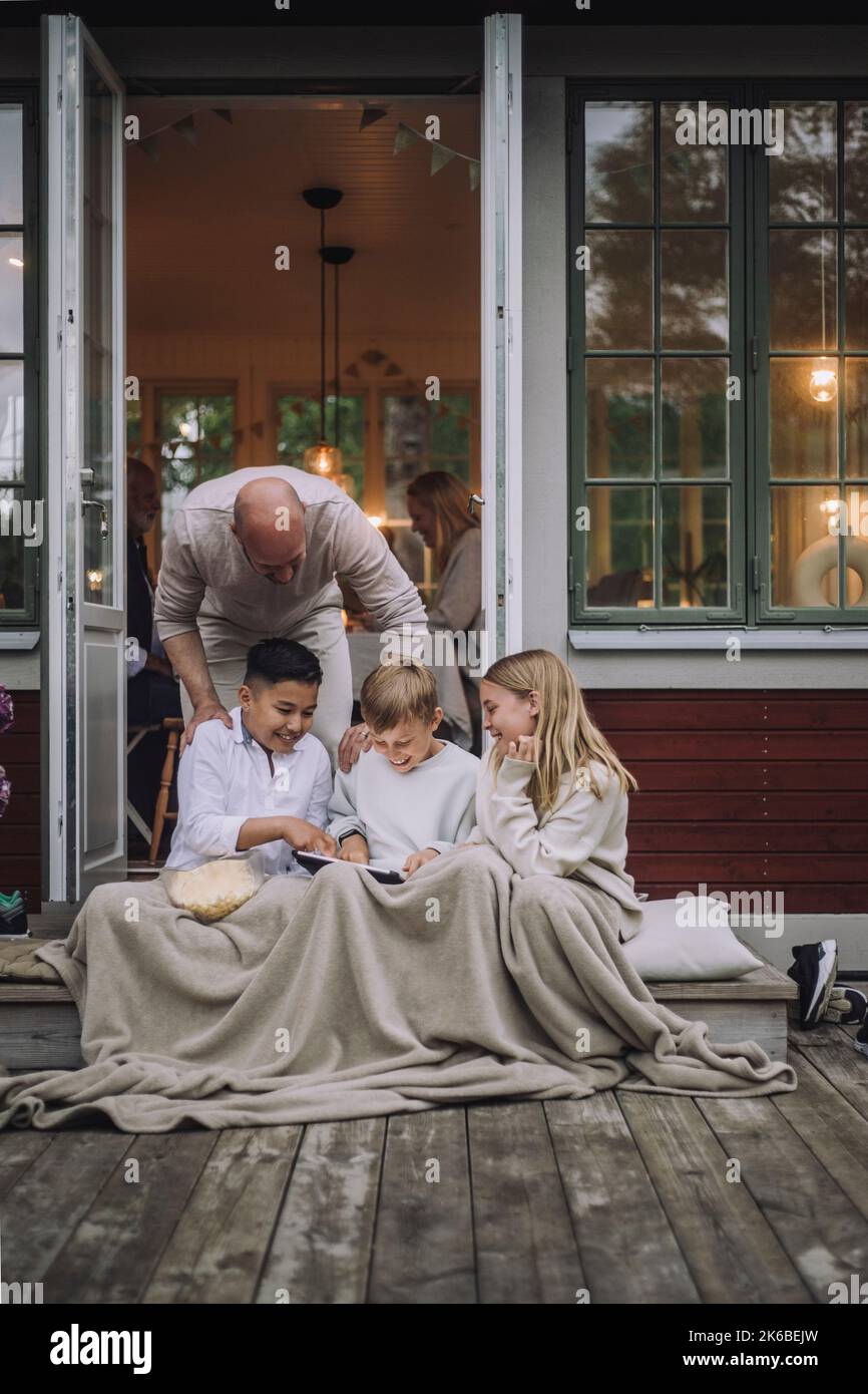 Man talking to children using digital PC while sitting on porch Stock Photo
