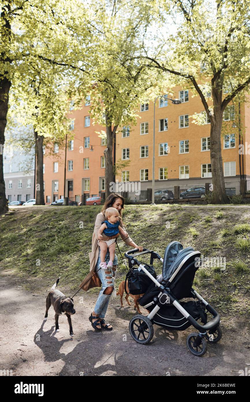 Mother with dogs carrying daughter while pushing baby stroller on