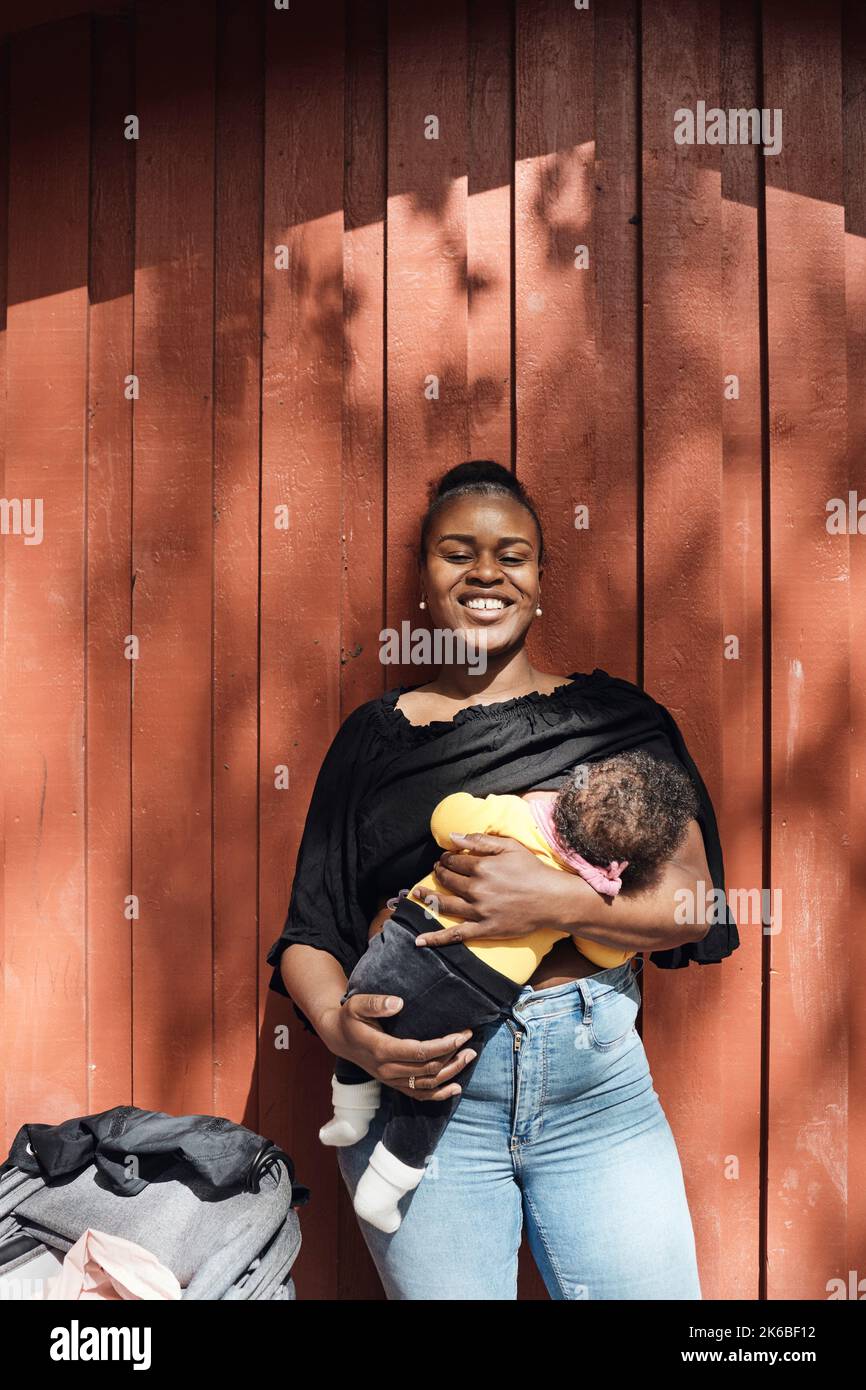 Happy woman breastfeeding toddler daughter in front of brown wall Stock