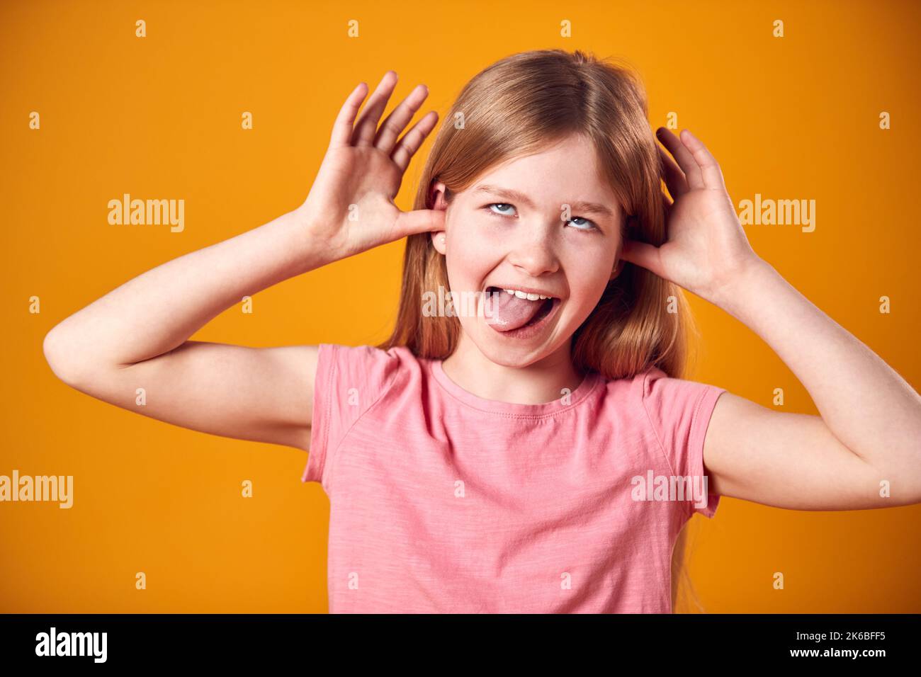 Studio Portrait Of Smiling Young Girl Pulling Funny Face Shot Against