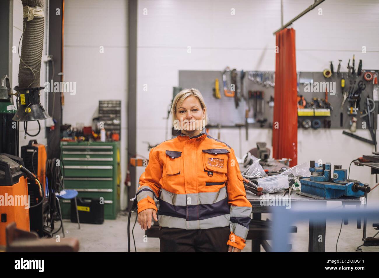 Portrait of smiling carpenter in reflective clothing standing in workshop Stock Photo
