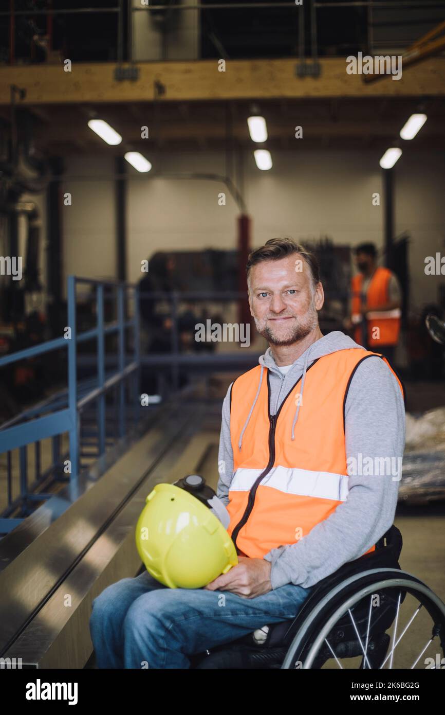 Portrait of smiling mature carpenter with hardhat sitting on wheelchair Stock Photo