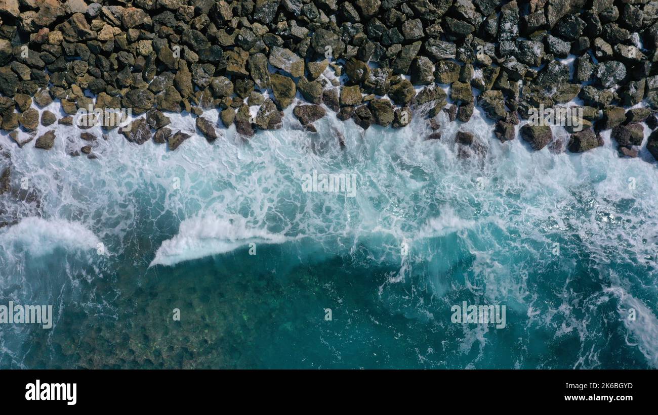 An aerial view of the beautiful blue splashing sea waves at a rocky ...