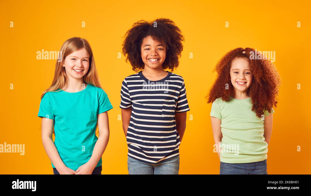 Studio Portrait Shot Of Three Children Friends Against Yellow Background Stock Photo