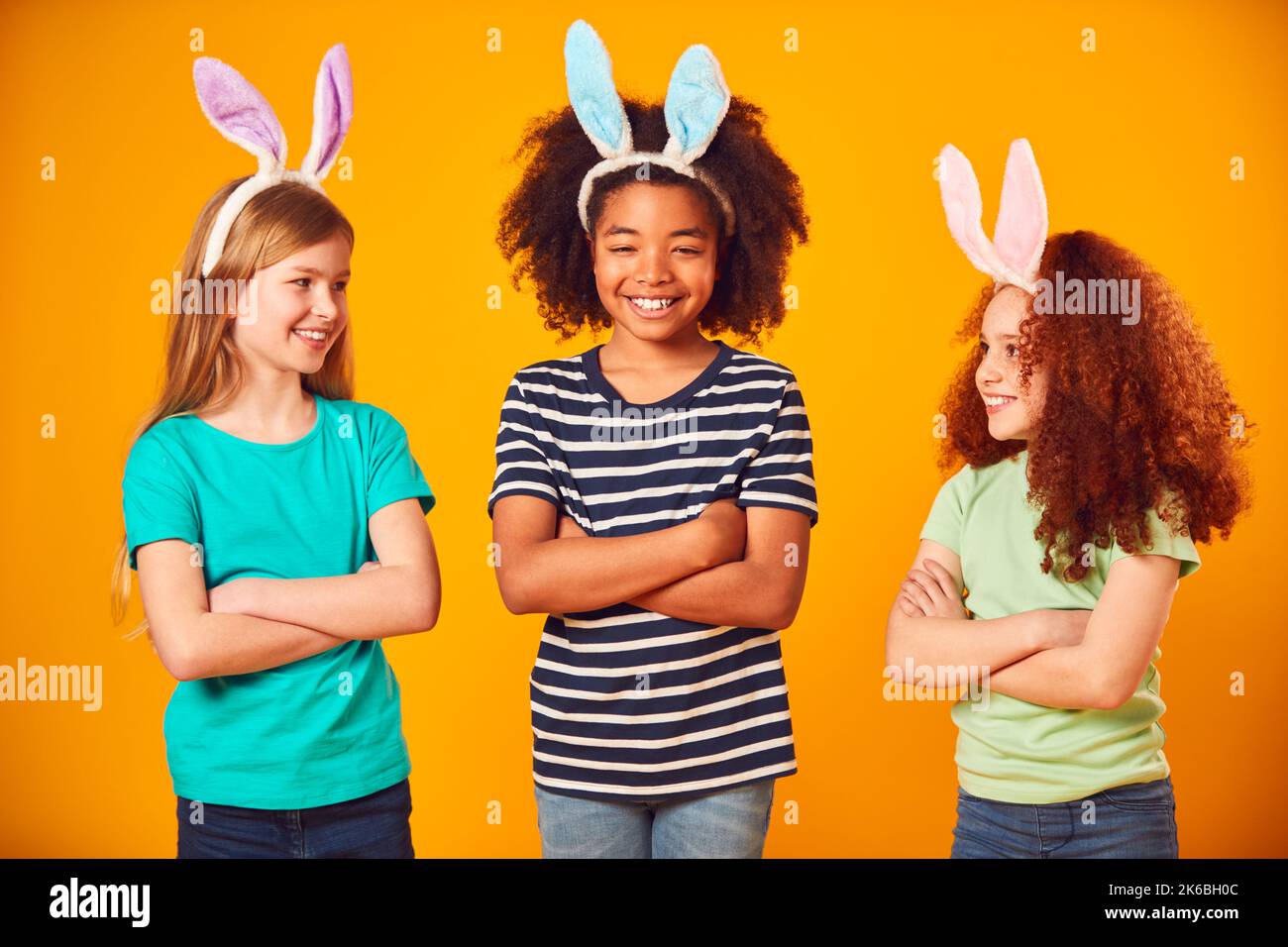 Studio Portrait Shot Of Three Children Friends Wearing Easter Rabbit Ears Against Yellow Background Stock Photo