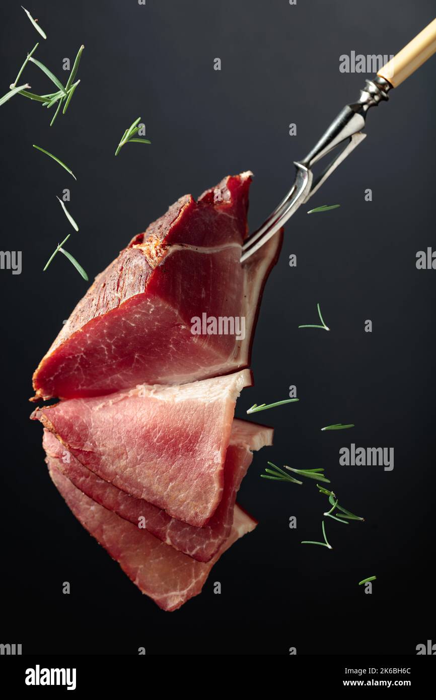 Drycured pork fillet sprinkled with rosemary on a black background