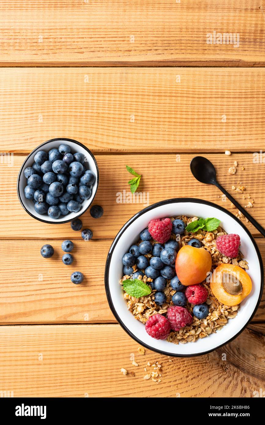 Crunchy dry oat honey granola with nuts and fresh berries in a bowl, wooden table background, top view copy space Stock Photo