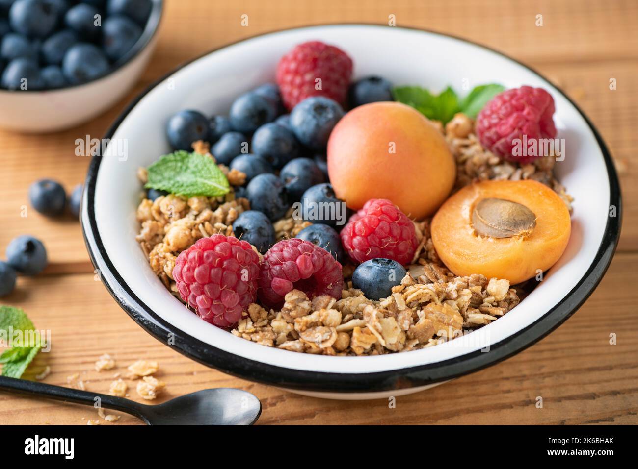 Crunchy oat honey granola with berries and fruits in bowl over wooden table background, closeup view Stock Photo