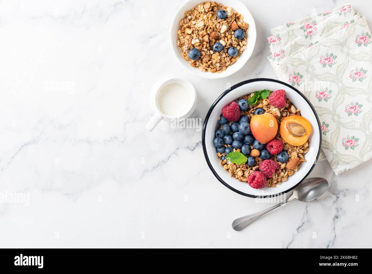 Crunchy Granola With Fresh Berries And Apricots In Bowl On White Marble Background, Top View Copy Space Stock Photo