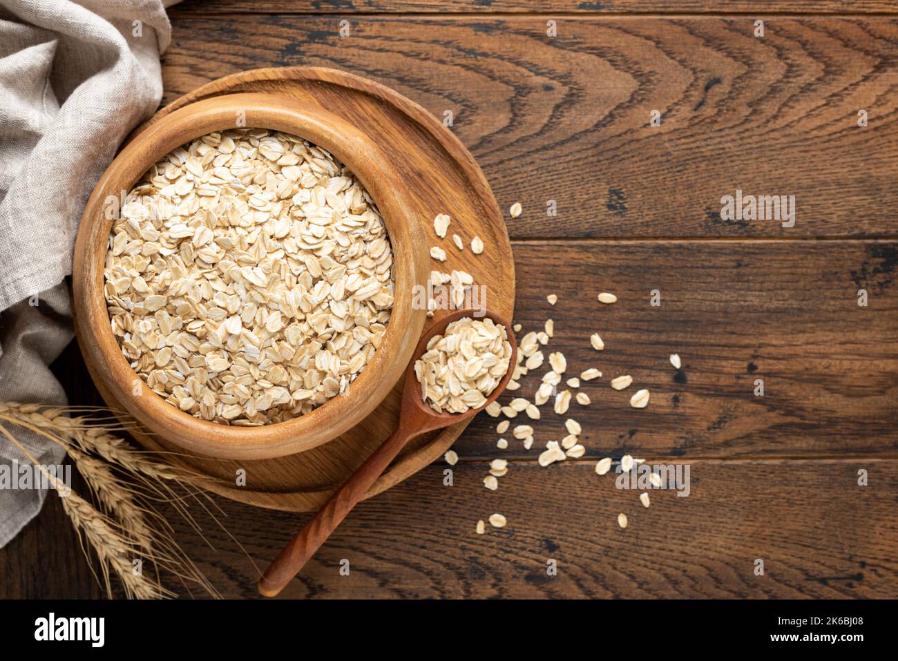 Rolled oats or oat flakes in wooden bowl on old wooden table background. Top view, copy space for text or design elements. Agriculture, healthy eating Stock Photo