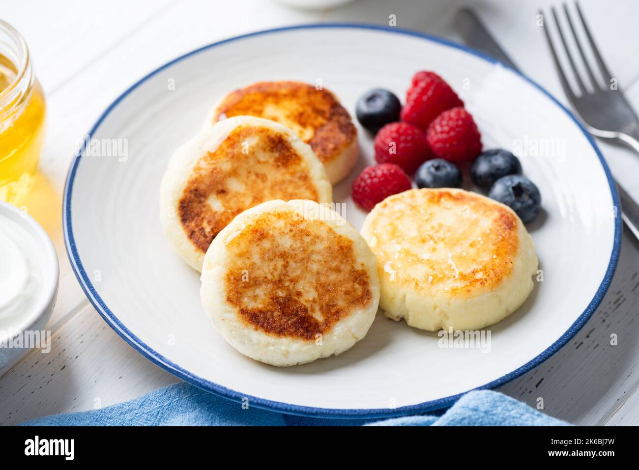 Cottage cheese fritters with berries and honey on plate, closeup view. Sweet breakfast food Stock Photo