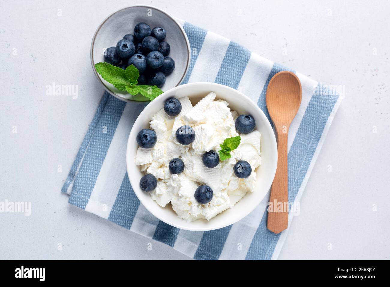 Cottage cheese, quark or curd in bowl served with blueberries on blue and white striped linen textile. Rich in calcium and protein dairy product, tabl Stock Photo
