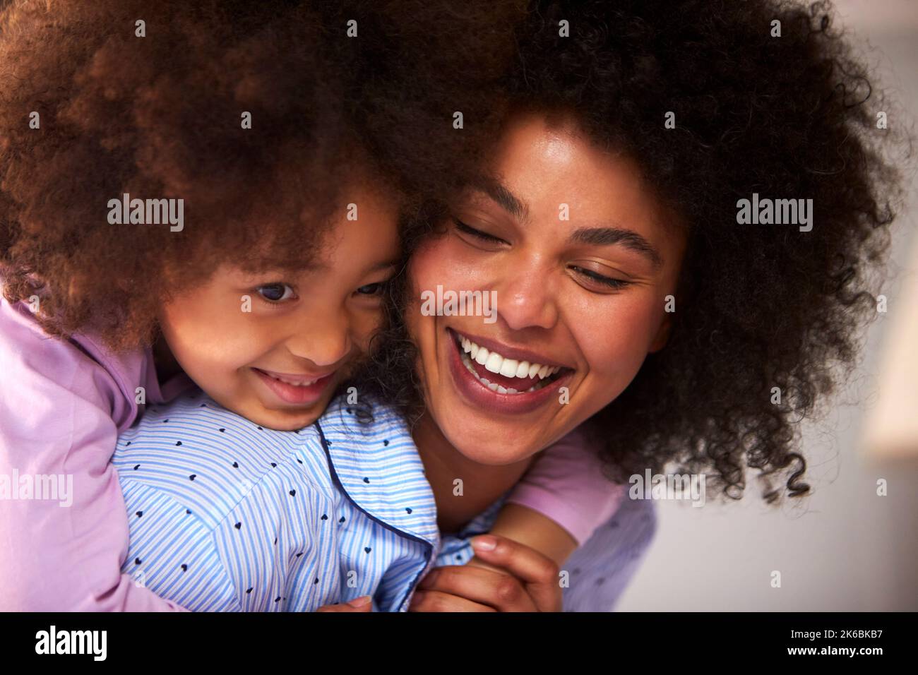 Mother And Daughter Wearing Pyjamas Playing On Bed At Home Together