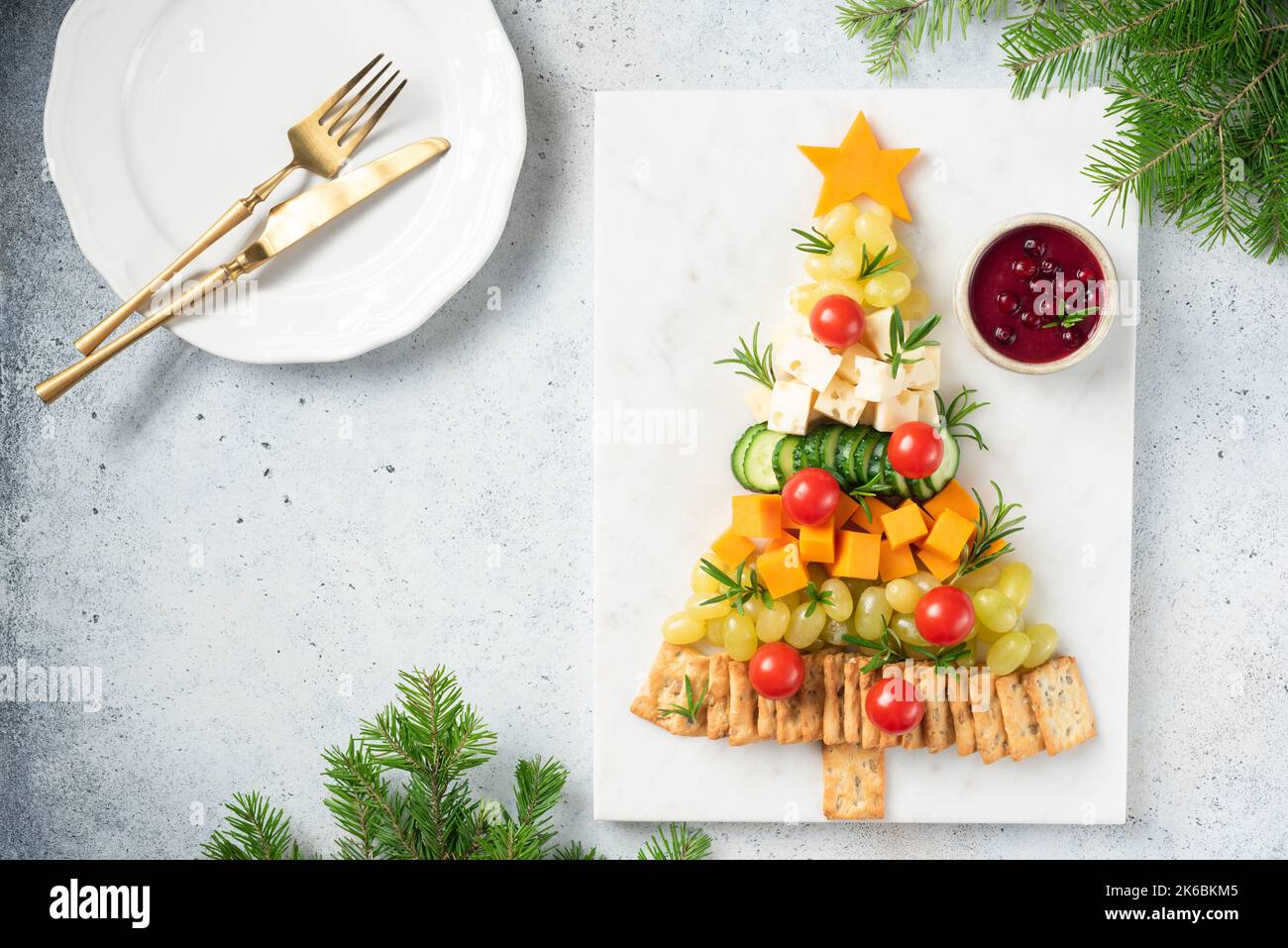 Christmas tree shaped Cheese Plate with crackers, grapes, cheese, tomatoes and cranberry sauce, winter holidays snack. Top view copy space Stock Photo